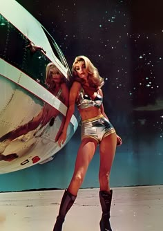 two women in short shorts and high heel boots standing next to an airplane with stars on the background