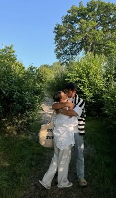 a man and woman kissing on the side of a dirt road in front of trees