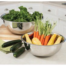 two metal bowls filled with vegetables on top of a counter next to cucumbers