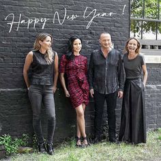 four people standing in front of a brick wall with the words happy new year written on it