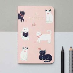 a pink notebook with cats on it next to a pencil and eraser set up