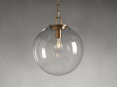 a clear glass globe light hanging from a brass chain on a gray wall with a white background