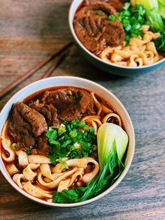 two bowls filled with meat and noodles on top of a wooden table