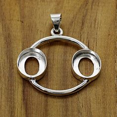 a silver pendant with two circles in the middle on a wooden surface and one circle has been cut out