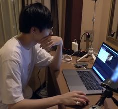 a man sitting in front of a laptop computer on top of a wooden desk next to a window