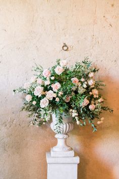 a white vase filled with lots of flowers on top of a table next to a wall