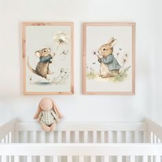 two framed pictures hang on the wall above a crib with a stuffed animal next to it