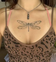 a woman with a dragonfly tattoo on her upper back shoulder and chest is wearing a brown tank top