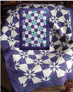 a purple and white quilt on a chair with a bookcase in the back ground