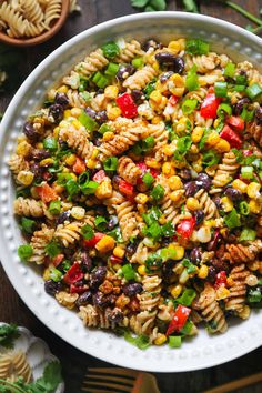 a white bowl filled with pasta salad on top of a table next to utensils