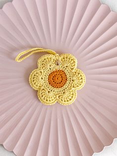 a crocheted flower ornament hanging from a pink paper plate on a white table