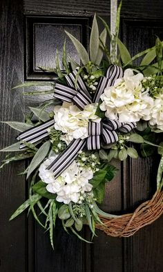 a wreath with white flowers and greenery hanging on a door