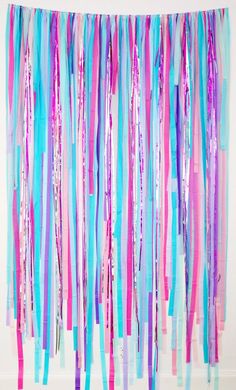 an abstract painting with pink, blue and purple streamers hanging from the ceiling in front of a white wall