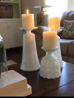 three candles sitting on top of a wooden table in front of a couch and coffee table