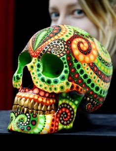 a woman looking at a brightly colored skull on a table with her face close to the camera