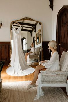 a woman sitting on top of a white chair in front of a dress hanging up