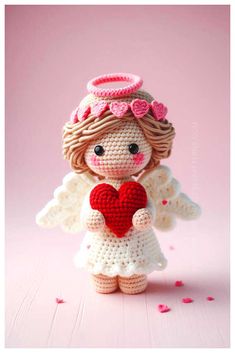 a crocheted angel holding a heart on top of a pink surface with confetti scattered around it