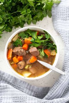 a bowl of soup with carrots, meat and parsley in it on a white surface