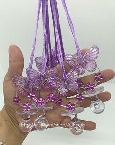 a hand holding several wine glasses with purple butterflies on them and beads hanging from the stems