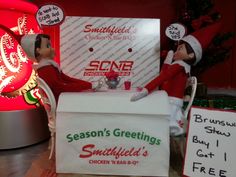 two elfs sitting at a table with signs on it and a sign that says season's greetings