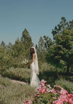 a woman in a wedding dress walking through some flowers