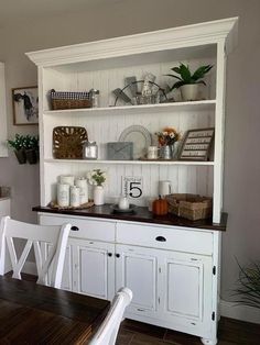 a dining room table with white chairs next to a hutch filled with pots and pans