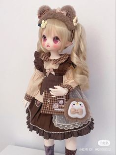 a doll with long blonde hair wearing a brown dress and holding a teddy bear in her hand