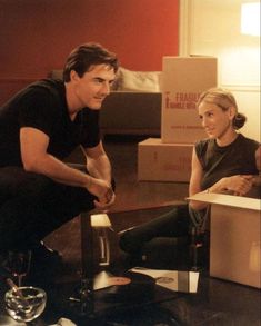 a man and woman sitting on the floor next to boxes