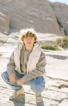 a woman squatting down in front of some rocks