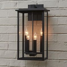 an outdoor wall light with three lit candles on the front and side of it, against a brick wall