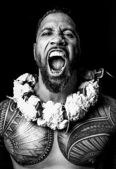 a man with tattoos on his chest is making a face and holding a flower lei around his neck