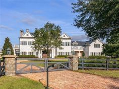 a large white house with a gate in front of it and brick walkway leading to the entrance