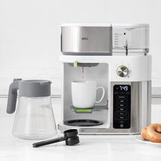 a coffee maker and some donuts on a white counter top next to a cup of coffee