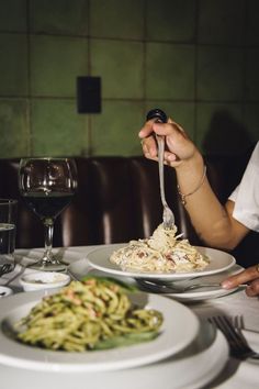 a woman is eating pasta with a fork at a table in front of a glass of wine