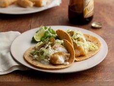 two tacos are sitting on a plate next to a bottle of beer and napkins