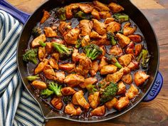 chicken and broccoli stir fry in a skillet on a wooden table next to a blue dish towel