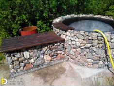 an outdoor fire pit made out of rocks with a hose connected to it and a bucket on the side