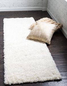 a white rug with two pillows on top of it next to a brick wall and wooden floor