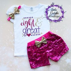 a white shirt and pink sequin shorts with a gold bow on the side, sitting next to a purple glitter skirt