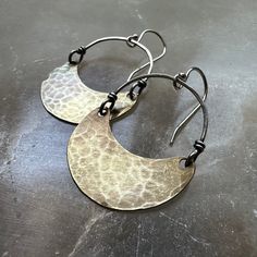 Over the years, my Crescent earrings have become our most popular and recognizable style! They are often the "first-pair" of earrings that people get for themselves or to gift another to start their collections. We make them in 4 sizes. Suspended from Sterling Silver wire and Sterling Silver earwires. Regardless of which size you choose, they are all amazingly lightweight and perfect as your "every day" earrings! Tiny = 3/4" wide x 1/2" tall & hang 1 3/8" from earwire to the bottom of the cresce Crescent Hammered Earrings, Hand Forged Earrings For Anniversary, Hand Forged Vintage Jewelry, Vintage Hand Forged Round Jewelry, Hand Forged Metal Earrings, Artisan Dangle Earrings For Anniversary, Pierced Metal Jewelry For Anniversary, Bronze Metal Jewelry For Anniversary, Brass Drop Earrings For Anniversary