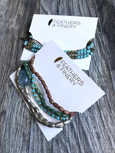 three bracelets with beads and charms on top of a wooden table next to a card