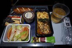 an airplane tray with food and drinks on it, including bread, salad, fruit, and other items