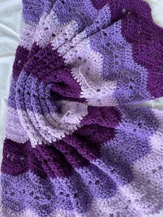 a purple and white crocheted blanket laying on top of a bed