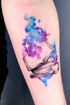 a watercolor tattoo with an open book and stars on it's left arm