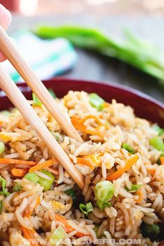 someone holding chopsticks over a bowl of rice and vegetables