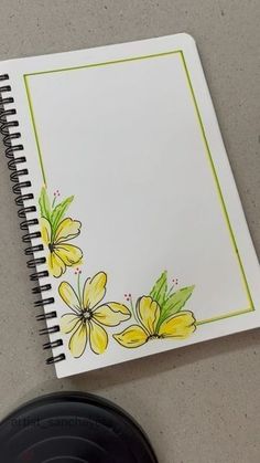 an open notebook with yellow flowers on it next to a black object and a pen