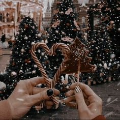 two hands holding candy canes in front of a christmas tree with snow falling on it