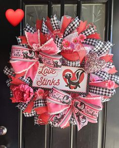 a valentine's day wreath on the front door with pink and black ribbon, red flowers and i love you stinks