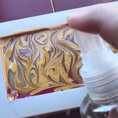 a person holding a bottle in front of a painting with gold and purple swirls on it