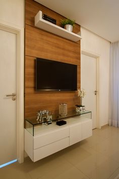 there is a television mounted on the wall in this living room with white cabinets and glass shelves